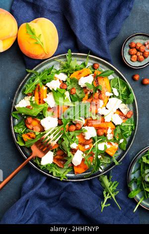 Salade d'été avec pêche grillée au fromage doux, noisettes et arugula sur fond de table bleu, vue du dessus, espace copie Banque D'Images