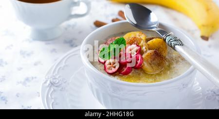 Faire cuire du porridge avec des bananes cuites, de la cannelle, de l'orange et des canneberges dans un bol en céramique pour un petit déjeuner sain sur fond clair.Mise au point sélective. Banque D'Images