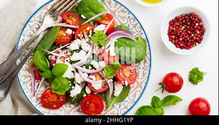 Tomates, feuilles d'épinards, oignons rouges et salade de feta sur une assiette en céramique légère.Mise au point sélective.Vue de dessus. Banque D'Images