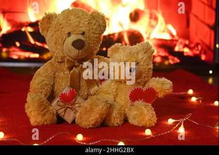 une paire d'ours en peluche est assise sur le fond d'un tissu tricoté rouge et d'une guirlande d'ampoules et tient deux coeurs rouges dans leur Banque D'Images