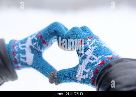 Mains en gants tricotés repliés en forme de coeur sur fond de neige.Déclaration d'amour, concept de la Saint-Valentin, temps d'hiver Banque D'Images