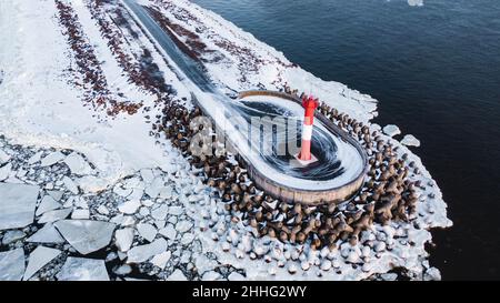 Vue aérienne d'un petit phare rouge dans la mer entouré de brise-lames couverts de glace et de flotteurs de glace autour Banque D'Images