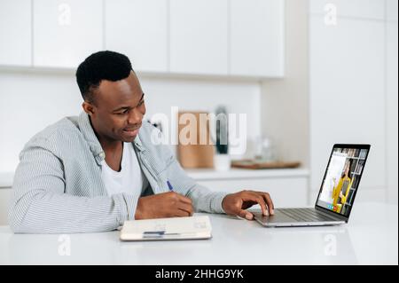 Formation en ligne à distance.Afro-américain intelligent gars, étudiant ou indépendant, assis à une table à la maison dans la cuisine, a une conférence en ligne, prend des notes, sur l'écran de la femme enseignant enseigne à distance Banque D'Images