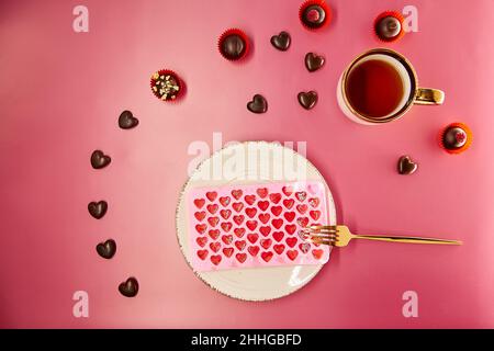 Coeurs en chocolat et bonbons décorés.Cœur de glace sur plaque vintage blanche avec fourchette et tasse de thé sur fond rose dégradé.Dîner romantique créatif, concept de la Saint-Valentin.Vue de dessus. Banque D'Images