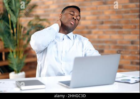 Homme d'affaires fatigué, stressé, directeur des ventes, assis à une table dans un bureau moderne, se massant le cou, débordé de négociations, travail dur et responsable, besoin de repos, de mal de tête Banque D'Images