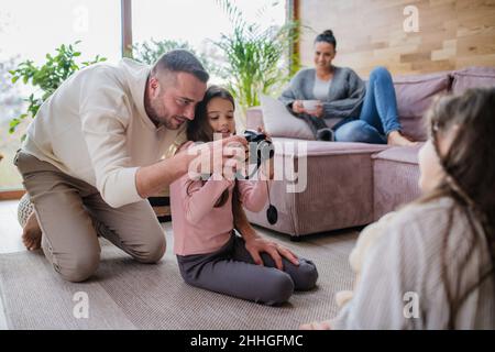Deux sœurs heureuses avec un père assis sur le sol et apprenant à utiliser l'appareil photo à la maison Banque D'Images