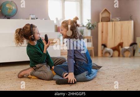 Petites filles avec casque et microphone prenant un entretien, s'amuser et jouer à la maison. Banque D'Images