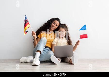 Cours de langue en ligne.Maman et fille avec ordinateur portable et bouquet de drapeaux Banque D'Images