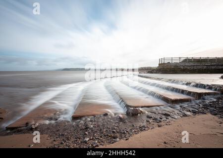 Longue exposition de la cascade de la rivière Avill qui coule sur la plage de Dunster dans le Somerset Banque D'Images