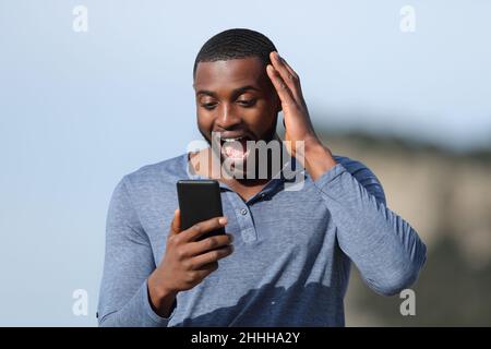 Un homme émerveillé avec une peau noire qui vérifie le smartphone à l'extérieur par beau temps Banque D'Images