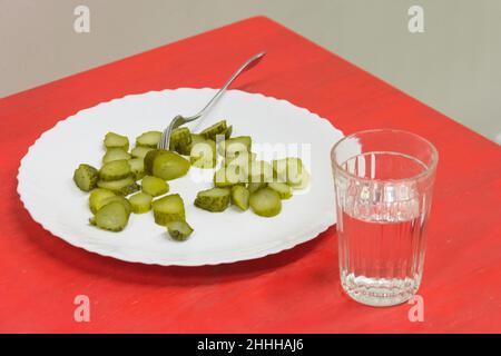 Morceaux hachés de concombres marinés sur une table rouge dans une assiette avec une fourchette et un verre de vodka Banque D'Images