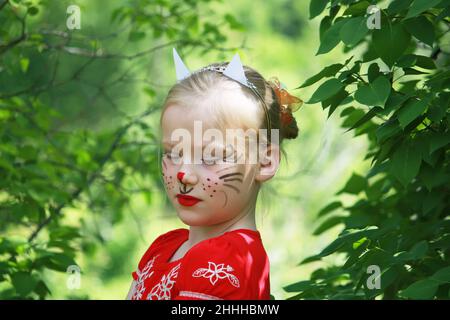 Belle heureuse souriante jeune blonde blanche fille avec visage peint comme un chat sur fond de nature d'été. Banque D'Images