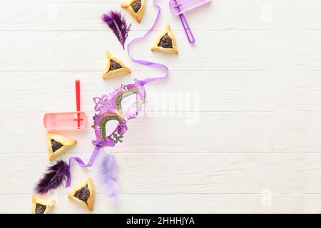 Masque de carnaval et biscuits Hamantaschen avec hochets pour les vacances de Purim sur fond de bois blanc Banque D'Images