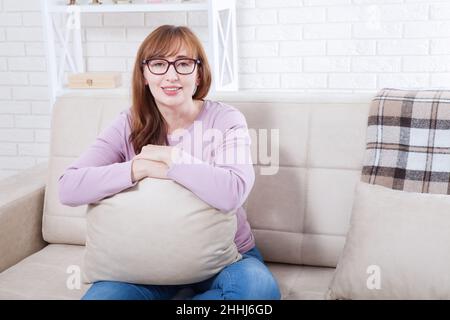 Belle femme d'âge moyen à la maison assise sur un canapé.Copier l'espace et la maquette Banque D'Images