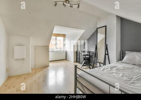 Une chambre moderne et lumineuse avec un lit double, un grand miroir et des équipements de bureau gris Banque D'Images