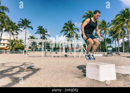 Accroupissez-vous dans une boîte d'entraînement à la salle de gym de la plage en plein air.Entraînement d'athlète d'homme au banc de fitness saut à l'extérieur de l'été american South Beach Miami ville Banque D'Images