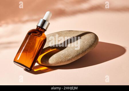 Huile essentielle sur une pierre de galet de rivière sur un fond beige.Produit de beauté médical cosmétique en bouteille de verre brun avec une pipette pour l'aromathérapie, al Banque D'Images