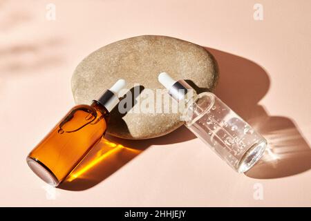Deux bouteilles compte-gouttes en verre sur une pierre de galet sur fond beige.Concept de cosmétiques naturels : acide hyaluronique, huile, sérum. Banque D'Images