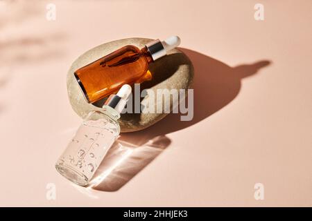 Deux bouteilles compte-gouttes en verre sur une pierre de galet sur fond beige.Concept de cosmétiques naturels : acide hyaluronique, huile, sérum. Banque D'Images