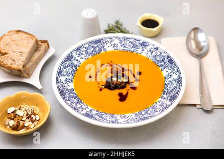 Soupe fraîche à la crème de potiron sur l'assiette avec des noisettes et de l'huile de potiron, servie avec du pain frais.Soupe de courge musquée prête à consommer sur fond neutre Banque D'Images