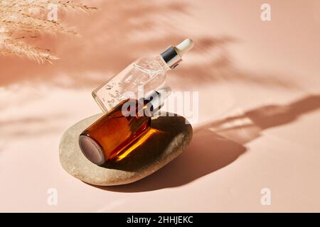 Deux bouteilles compte-gouttes en verre sur une pierre de galet sur fond beige.Concept de cosmétiques naturels : acide hyaluronique, huile, sérum. Banque D'Images
