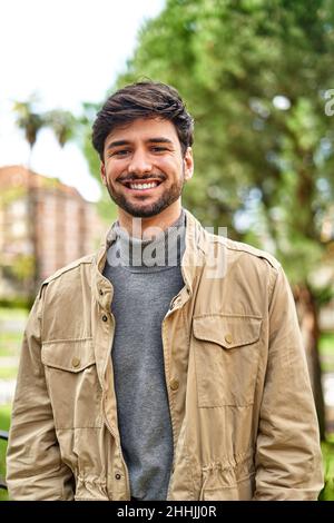 Joyeux homme barbu dans un col de cygne décontracté et veste souriant gaiement à la caméra dans le parc vert Banque D'Images