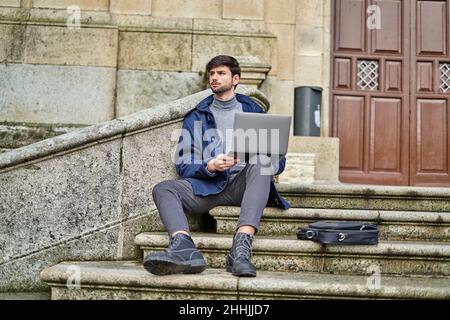 Un étudiant assis sur un escalier en pierre et naviguant sur un netbook tout en se préparant à une tâche universitaire Banque D'Images