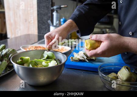 Un mâle méconnaissable fait cuire dans un artichaut frais uniforme près d'un bol au-dessus de la table pendant qu'il travaille au restaurant Banque D'Images