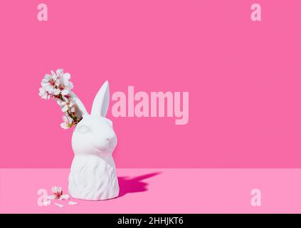 Buste d'un lapin blanc avec fleurs d'amande sur fond rose Banque D'Images