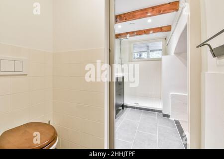 wc rom avec cuvette et porte menant à une salle de bains carrelée avec cabine de douche et lampes lumineuses au plafond Banque D'Images