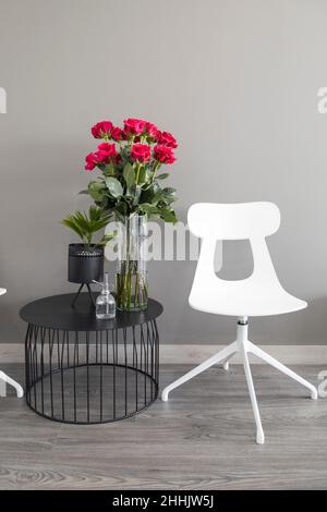 chaise à côté d'une table avec un vase moderne avec un bouquet de roses rouges, décoration avec fleurs fraîches à l'intérieur de la maison, meubles Banque D'Images