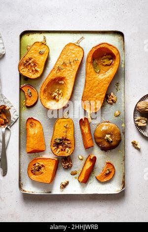 Vue de dessus des tranches de délicieux citrouilles rôties maison avec des noix sur une plaque de cuisson en métal placée sur une table dans une cuisine légère Banque D'Images