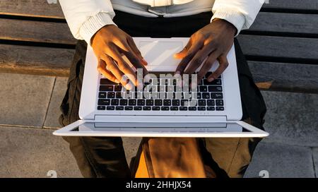 Depuis le haut, un travailleur indépendant afro-américain méconnu, assis sur un banc dans le parc et naviguant sur un ordinateur portable tout en travaillant à distance par temps ensoleillé Banque D'Images