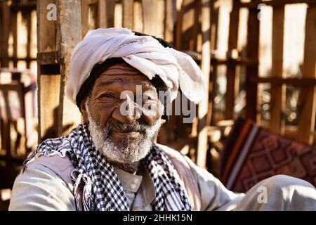 Homme nubien âgé dans une tenue ethnique assis sur un tapis dans la cour et regardant la caméra au soleil Banque D'Images