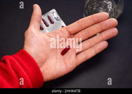 Personne prenant des médicaments avec fond noir avec une plaquette thermoformée et de l'eau. Banque D'Images