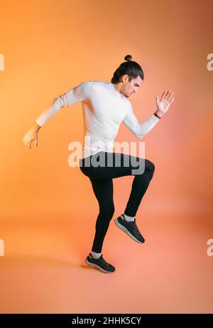Vue latérale d'un jeune athlète ethnique motivé avec de longs cheveux foncés dans des vêtements de sport faisant de l'exercice de course sur fond orange Banque D'Images