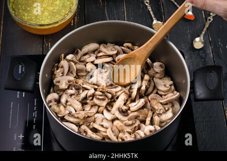 De dessus de la récolte personne méconnaissable avec une cuillère en bois remuant les champignons dans la casserole tout en cuisant la soupe sur le poêle à induction dans la cuisine Banque D'Images