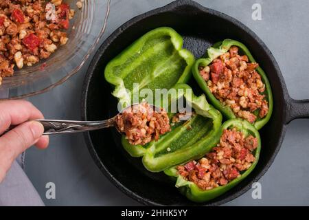 De dessus de la récolte personne sans visage mettant la farce de pizza avec du boeuf dans les poivrons verts dans la poêle à frire tout en cuisinant dans la cuisine Banque D'Images