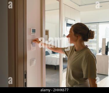 Vue latérale d'une femme de campagne en train de mettre la clé de carte dans le commutateur dans une chambre d'hôtel moderne en journée Banque D'Images