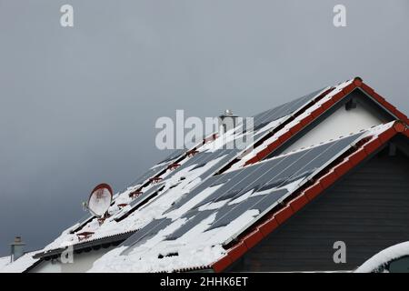 Toit carrelé de la maison avec panneaux solaires couverts de neige en hiver Banque D'Images