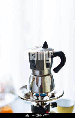 Moka moderne en métal pour préparer du café placé sur un poêle à gaz inoxydable dans une cuisine légère avec des tasses sur fond flou Banque D'Images