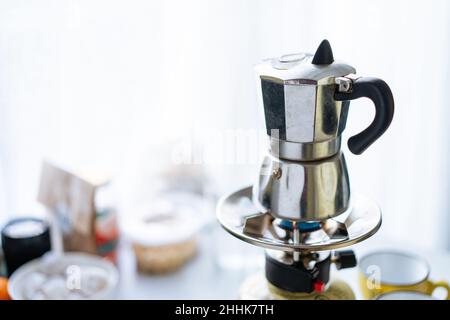 Moka moderne en métal pour préparer du café placé sur un poêle à gaz inoxydable dans une cuisine légère avec des tasses sur fond flou Banque D'Images