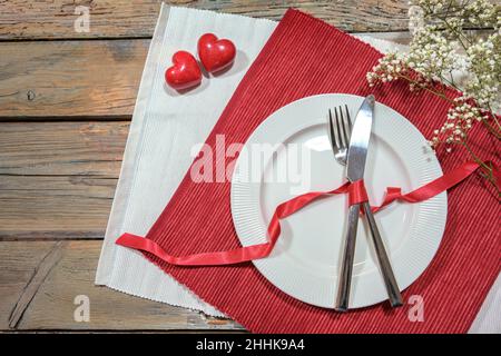 Table pour un dîner romantique avec deux coeurs, plat et couverts sur des serviettes rouges et blanches, concept amour, table rustique en bois avec espace copie, hig Banque D'Images