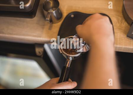 Grand angle de récolte anonyme Barista falsification du café aromatique moulu dans le porte-filtre sur le tapis d'autosurveillance en travaillant au comptoir Banque D'Images