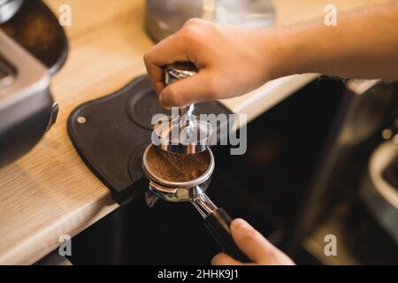 Grand angle de récolte anonyme Barista falsification du café aromatique moulu dans le porte-filtre sur le tapis d'autosurveillance en travaillant au comptoir Banque D'Images