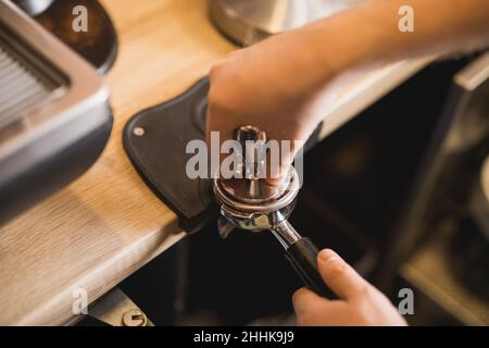 Grand angle de récolte anonyme Barista falsification du café aromatique moulu dans le porte-filtre sur le tapis d'autosurveillance en travaillant au comptoir Banque D'Images