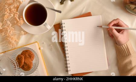 Photo aérienne, Une femme en chandail confortable esquissant sur du papier pour ordinateur portable.Compositions d'espace de travail confortables et féminines. Banque D'Images