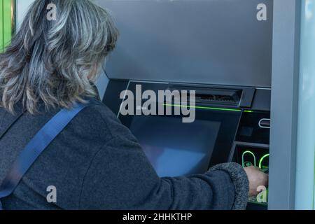 femme aux cheveux blancs et à la fourrure grise obtenant de l'argent de la machine à billets Banque D'Images