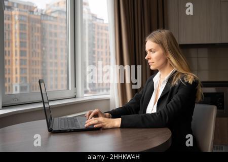 Femme d'affaires caucasienne sérieuse motivée travaillant dans un bureau lumineux avec un ordinateur portable près de la fenêtre, une femme millénaire dans un costume élégant crée un nouveau Banque D'Images