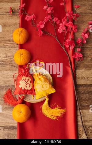 Mandarines, branche de pêche en fleur et petits sacs-cadeaux rouges et jaunes avec broderie bonne chance Banque D'Images